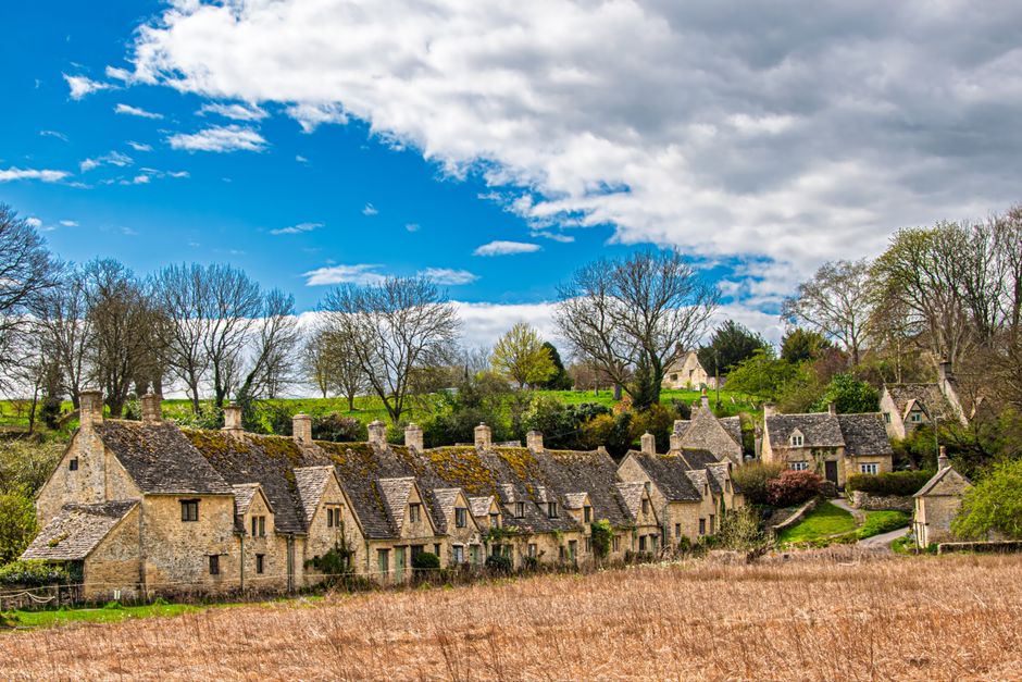 Eine Panoramaansicht der englischen Landschaft in den Cotswolds, sanft geschwungene grüne Hügel, honigfarbene Steinhäuser und...