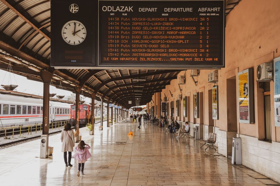 La bacheca delle partenze in una grande stazione inglese che mostra servizi intercity, i viaggiatori controllano i binari sottostanti
