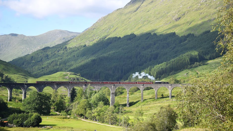 Glenfinnan-viadukt Skotlannin ylänköalueella, jota höyryauto ylittää, ympärillä vihreät kukkulat ja järvi
